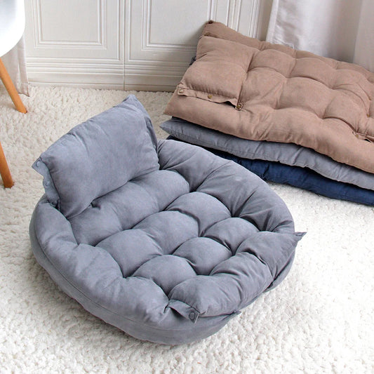 Gray pet bed on a white carpet with folded blankets in the background