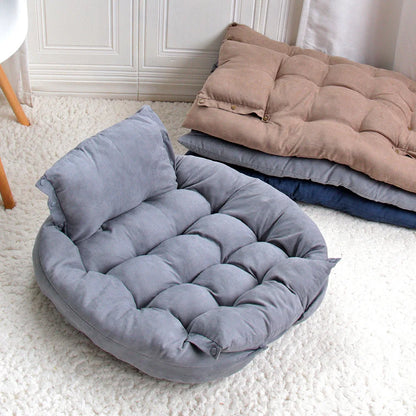 Gray pet bed on a white carpet with folded blankets in the background
